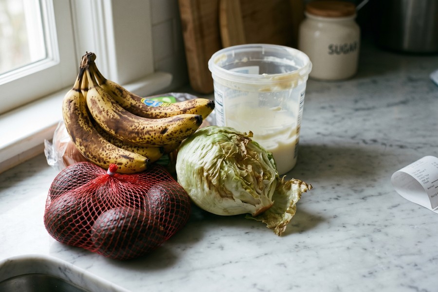 Weekly meal plan written on a notepad beside a grocery list and fresh produce on a kitchen counter