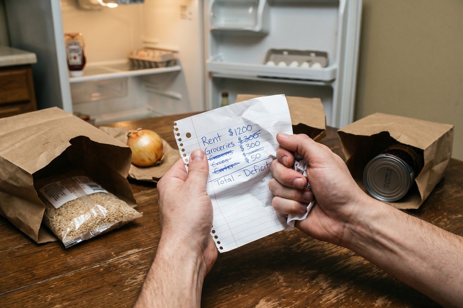 Person comparing grocery receipt to a monthly food budget worksheet at kitchen table