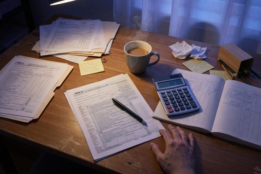 Gig worker calculating monthly expenses on a phone with calculator and receipts
